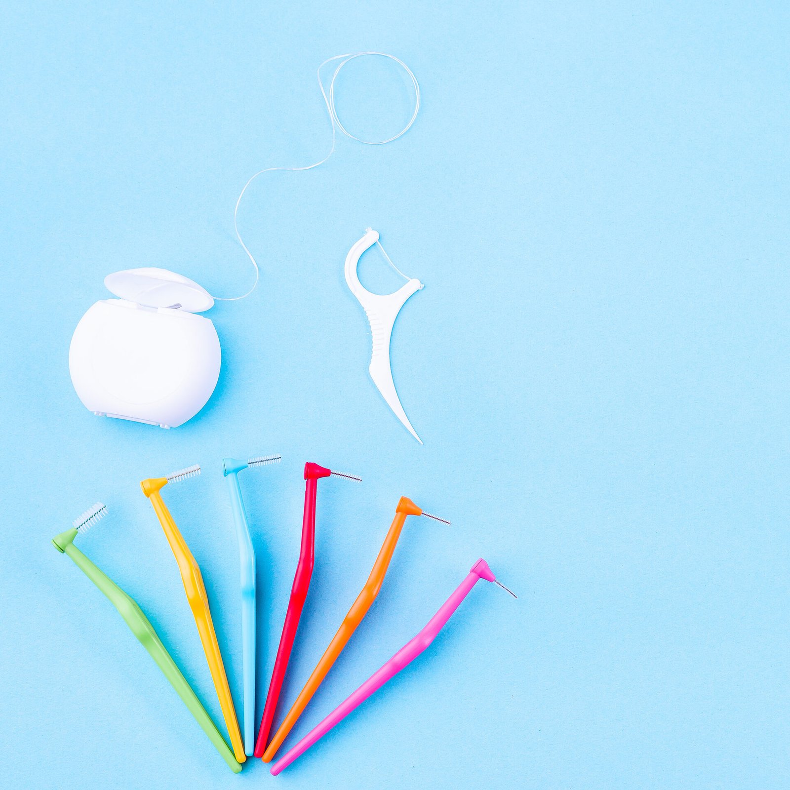 Produtos de higiene oral, incluindo fio dentário e escovilhões interdentários, sobre fundo azul